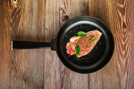 raw red appetizing meat steak of pork, cow, lamb with spices in a pan. Wooden background.の写真素材