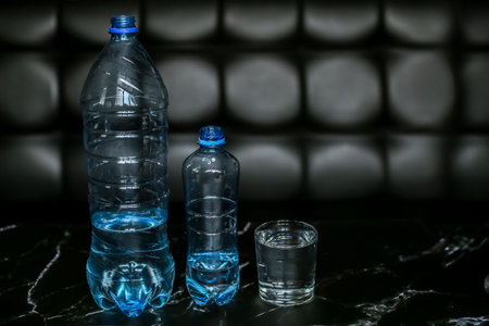 Two blue water bottles and a glass with clean drinking water on a black background