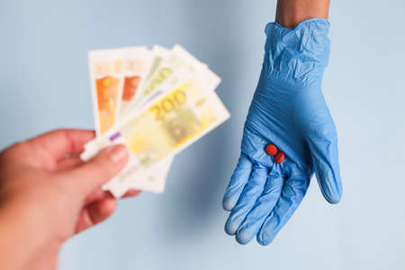 A doctors hand in a blue medical glove holds pills, and the patients hand holds out euro money to him for a fee for medicines.の写真素材