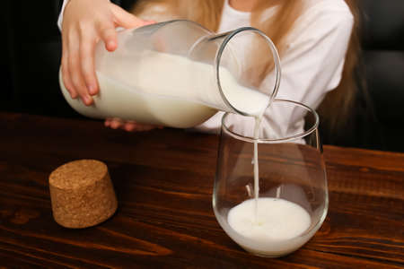 Girl pours milk from a bottle into a glass, a source of calciumの写真素材