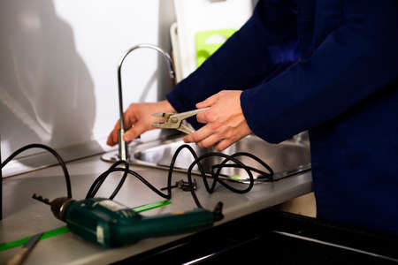 Plumber in uniform installing and repairing a faucet in the kitchen, close upの写真素材
