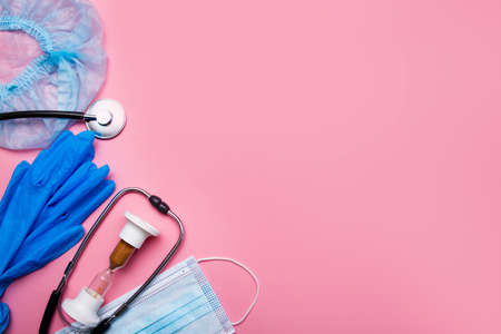 Items for the doctor injection syringe, gloves, protective mask and hourglass, stethoscope on a pink background with copy space.の写真素材