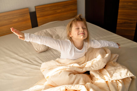 The girl sits on the bed in the early morning sun and stretches, the energy of good morning, good healthy sleep.の写真素材