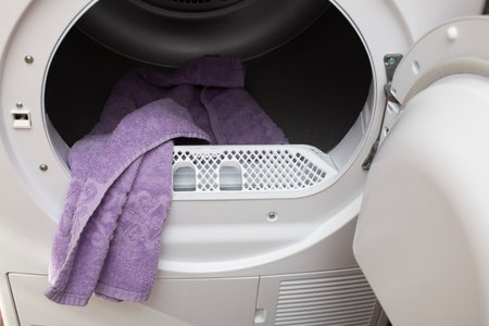The open door of a modern front-loading tumble dryer. There is a dry towel inside.