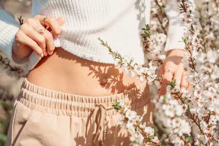 Partial view of beautiful slender woman in delicate clothes posing with hands near her belly and...