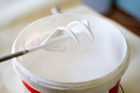 White paint in bucket with work tool mixer on the floor. Bucket with white paint indoors. Home improvement concept.の写真素材
