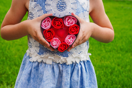 Close-up of kids hands holding a gift in a pink heart, presents for valentines day, birthday,...