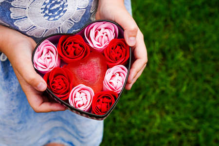 A box in a heart with soap roses in the hands of a little girl. Mothers day gift love, present for loving people. Celebration date, valentines day cardの写真素材
