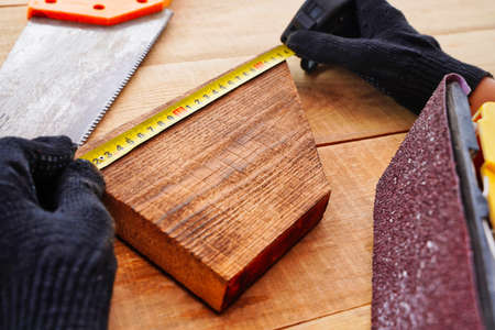 Carpenter measuring wooden plank at workplace with gloves. Making handmade products from wood.の写真素材
