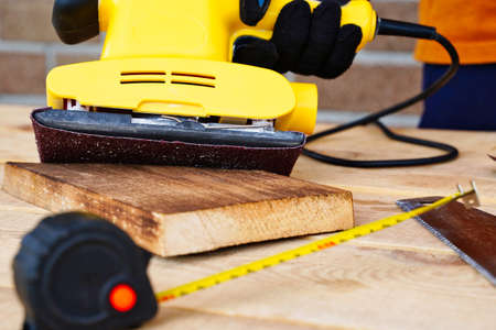 Carpenter worker working with wood, sanding and removing the top layer with a sander. Surface polishing for smoothnessの写真素材