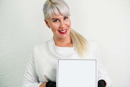 Portrait of a smiling beautician, doctor in a white coat, holding an empty blank, a white box with a place for your text, copy spice, advertising of products for face and skin careの写真素材