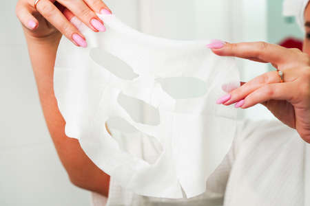 Face Skin Care moisturizing Korean cosmetics concept. Portrait Of Beautiful woman Removing White Sheet Mask From Healthy Fresh Skin. Cloth Mask On Facial Skin.の写真素材