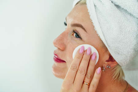 A woman removes makeup with a napkin in the bathroom, wipes her face with a cotton pad. Cleansing and moisturizing for aging skin, care and moisturizingの写真素材