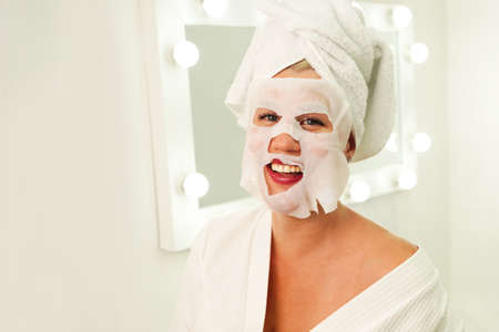 Skin care and beauty concept. Moisturizing mask. Anti aging procedure. Woman applying sheet mask on her faceの写真素材