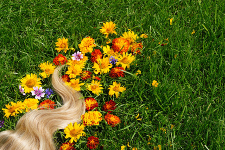 A lock of blond hair among the flowers, on the green grass. Hair health concept, natural ingredient...