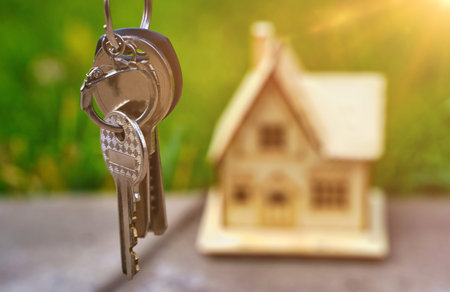 Close-up keys in focus on the background of a blurred wooden house, the concept of renting, selling or buying real estate. Investing in the construction of a country house.の写真素材