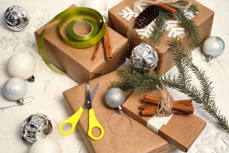 Wrapping christmas holiday handmade present in craft paper with twine ribbon. Making bow at xmas gift box, decorated with snowflake on white table, top view.の写真素材