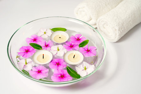 Burning floating candles with pink flowers in a bowl of water and two white towels, spa relaxation, body care and wellnessの写真素材