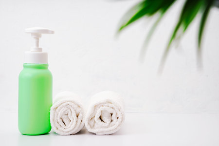 Green bottle of moisturizing lotion and two white cleanliness towels in the bathroom. Body and skin care concept. Copy spaceの写真素材