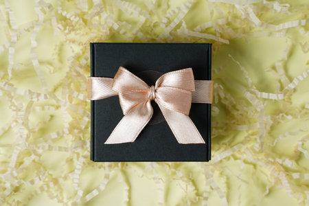 Dark gift present box with ribbon and bow on yellow background top view copy space. Flat lay holiday...