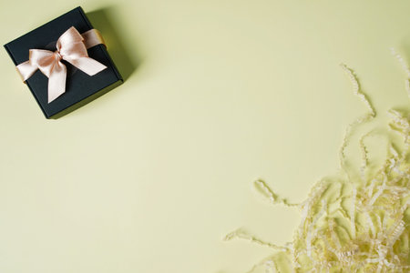 Black gift box with a golden ribbon and a large bow on a light yellow background. Place for the...