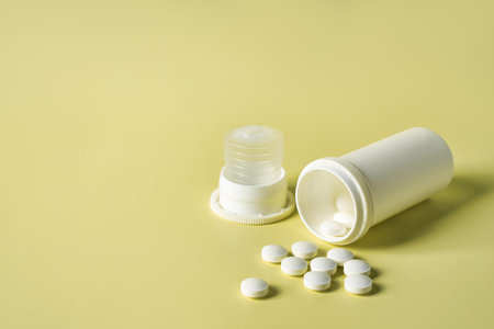 close up bottle of pills with medicinal white tablets on yellow background