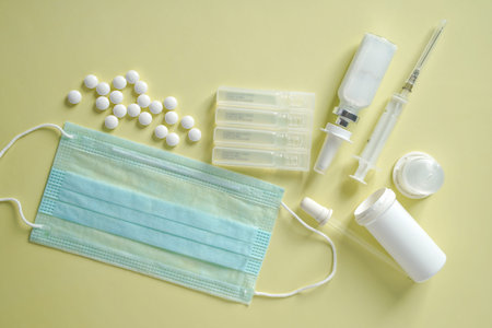 Medical blue mask, ampoule vials, tablets, nasal spray and syringe on light background