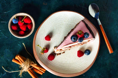 A piece of cake, chocolate biscuit with cream cheese filling on dark blue background close up. Berries on pink cream decoration.の写真素材