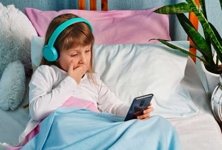 Happy cute little vlogger chatting looking at camera, talking to webcam, smiling, girl making online video call, recording video blog, sitting on bed at home, portraitの写真素材