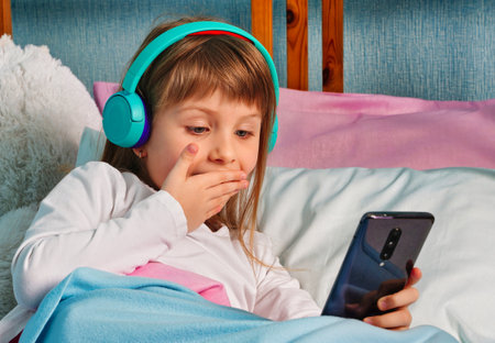 Happy cute little vlogger chatting looking at camera, talking to webcam, smiling, girl making online video call, recording video blog, sitting on bed at home, portraitの写真素材