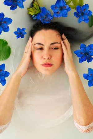 The woman takes a wellness bath filled with milk with copy space. The buds of blue flowers float on...