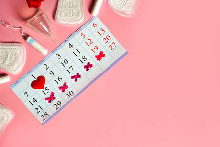 Menstruation days products, red heart and calendar with red marked dates of menstruation on pink background with copy spaceの写真素材