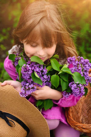 Child girl in lilac Garden. Girl smells the flowers, inhale the aroma in springtime. Gardening.の写真素材