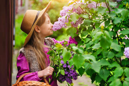 Beautiful girl in straw hat in lilac Garden. Girl with lilac flowers in springtime. Gardening.の写真素材