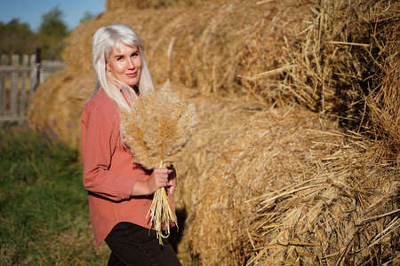 Beauty rustic girl outdoors, enjoying nature, rural sunlight. The glow of the sun. girl collects a bouquet of wildflowers. Tinted in warm colors. Autumn.の写真素材