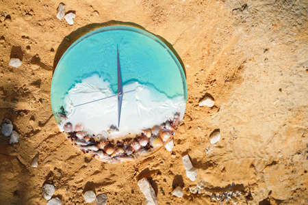 An alarm clock with seashells sitting on the sand with water, vacation time. Beach Timeの写真素材