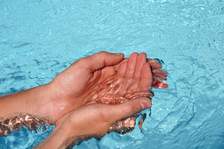 The hands cupped together submerged in clean clear blue water in swimming pool