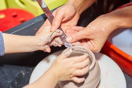 Teacher and kid making ceramic pot on pottery wheel. Modeling of clay on a potter's wheel In the pottery workshopの写真素材