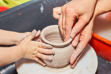Teacher and kid making ceramic pot on pottery wheel. Modeling of clay on a potter's wheel In the pottery workshopの写真素材