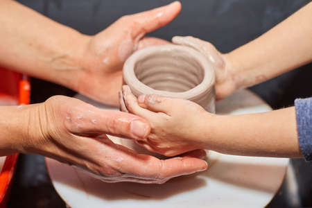 Teacher and kid making ceramic pot on pottery wheel. Modeling of clay on a potter's wheel In the pottery workshopの写真素材