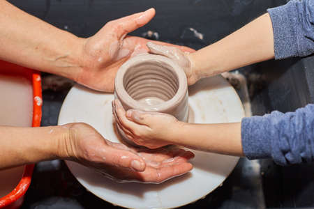 Teacher and kid making ceramic pot on pottery wheel. Modeling of clay on a potter's wheel In the pottery workshopの写真素材