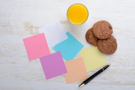 Blank notepad and glass of juice with cookies on office wooden tableの写真素材
