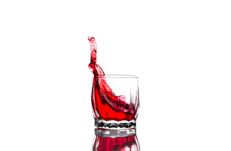 Splash of red juice, wine in a glass ribbed whiskey glass on a white backgroundの写真素材