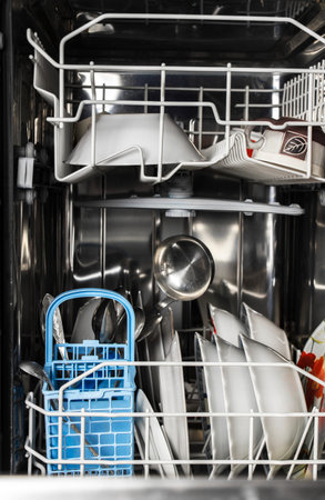 Dishwasher detail. An opened dishwasher with trays extended, lightly loaded. Inside A Dishwasher