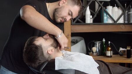 Young barber trimming beard of male clientの写真素材