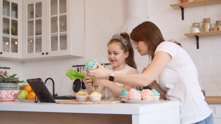 Young mother and little daughter icing cupcakesの写真素材