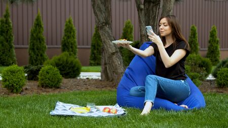 Young woman photographing fruits and sandwich in gardenの写真素材