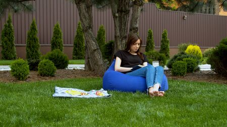 Young woman reading book in garden with cap of coffeeの写真素材