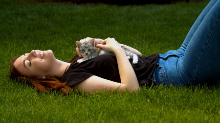 Young woman stroking kitten in garden grassの写真素材