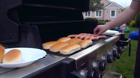 Person turning sausages for hot dog on grillの写真素材